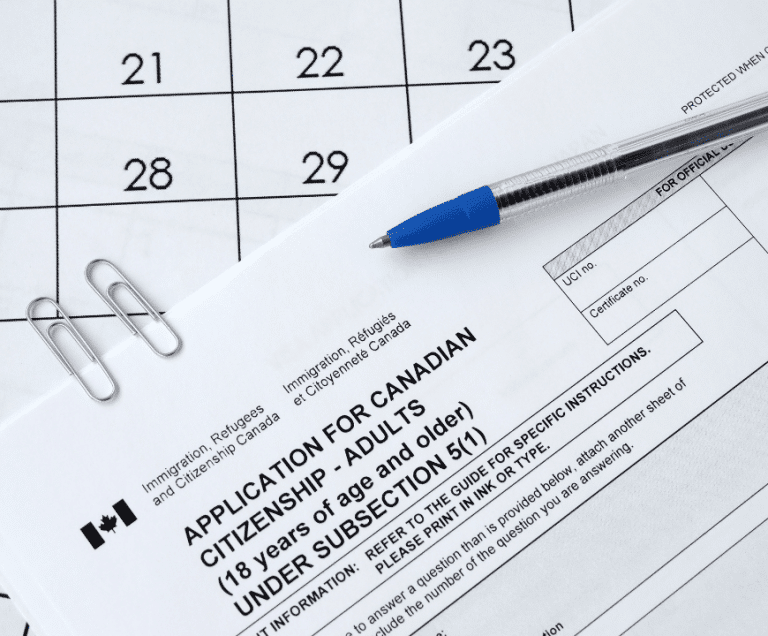 Canadian citizenship application form for adults, a blue pen, and two paper clips on a white surface. The form is partially filled out and titled “Application for Canadian Citizenship - Adults.”.