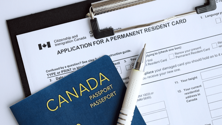Canadian passport and pen resting on an Application for a Permanent Resident Card form from Citizenship and Immigration Canada, clipped to a clipboard.